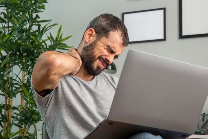 hombre frente a la computadora con dolor muscular